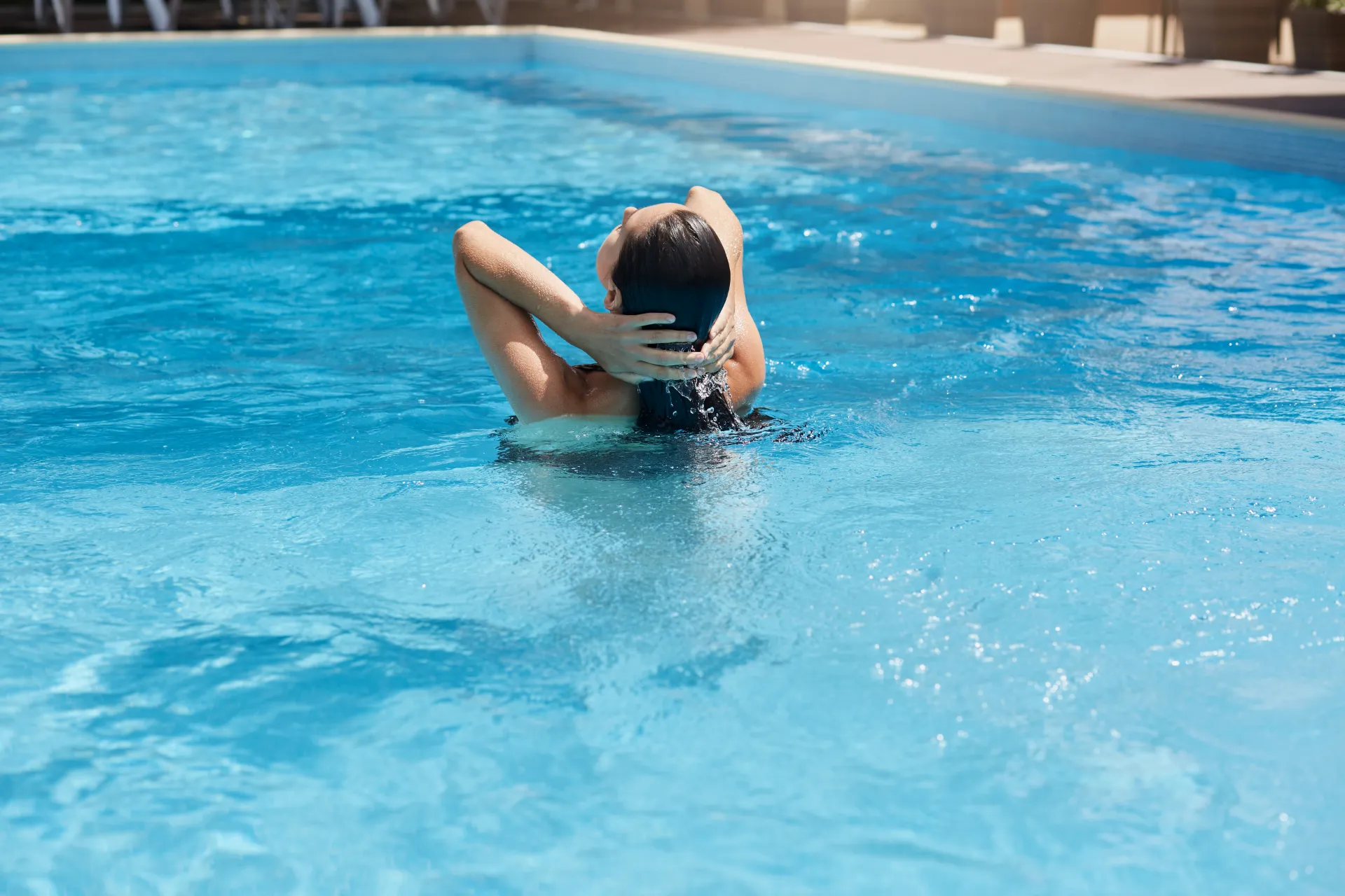 young-woman-posing-backwards-while-standing-blue-water-touching-her-wet-dark-hair