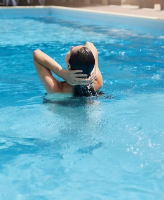 young-woman-posing-backwards-while-standing-blue-water-touching-her-wet-dark-hair
